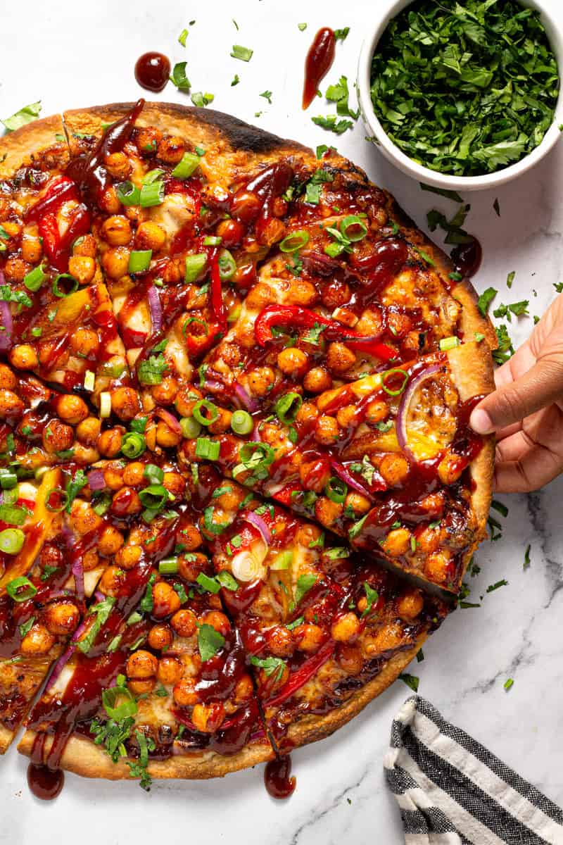 A small hand reaching for a slice of barbecue chickpea pizza garnished with fresh cilantro 