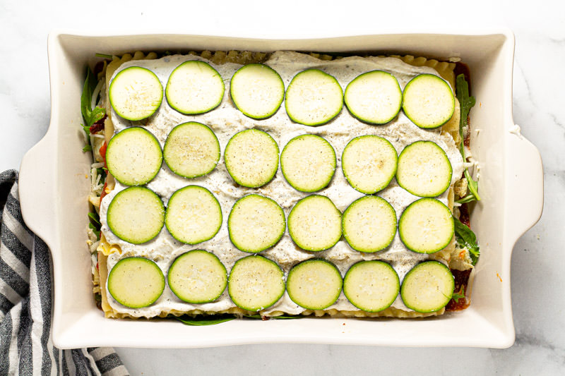 Photos showing how to layer Mediterranean lasagna in a large white baking dish 