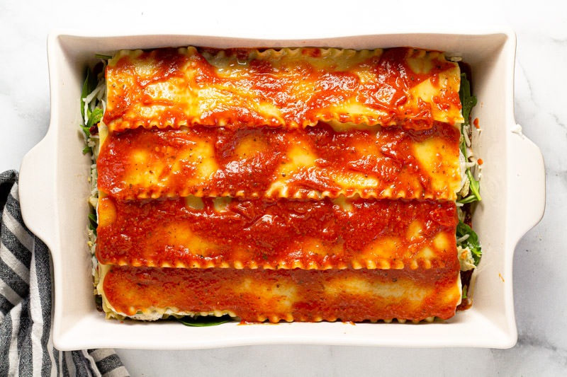 Photos showing how to layer Mediterranean lasagna in a large white baking dish 
