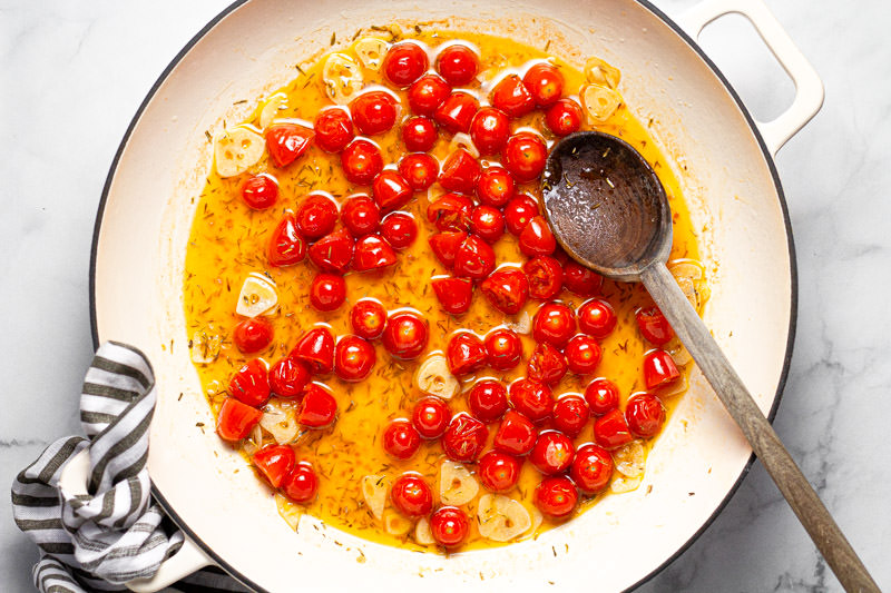 Large white pan with sauteed tomatoes in olive oil and white wine