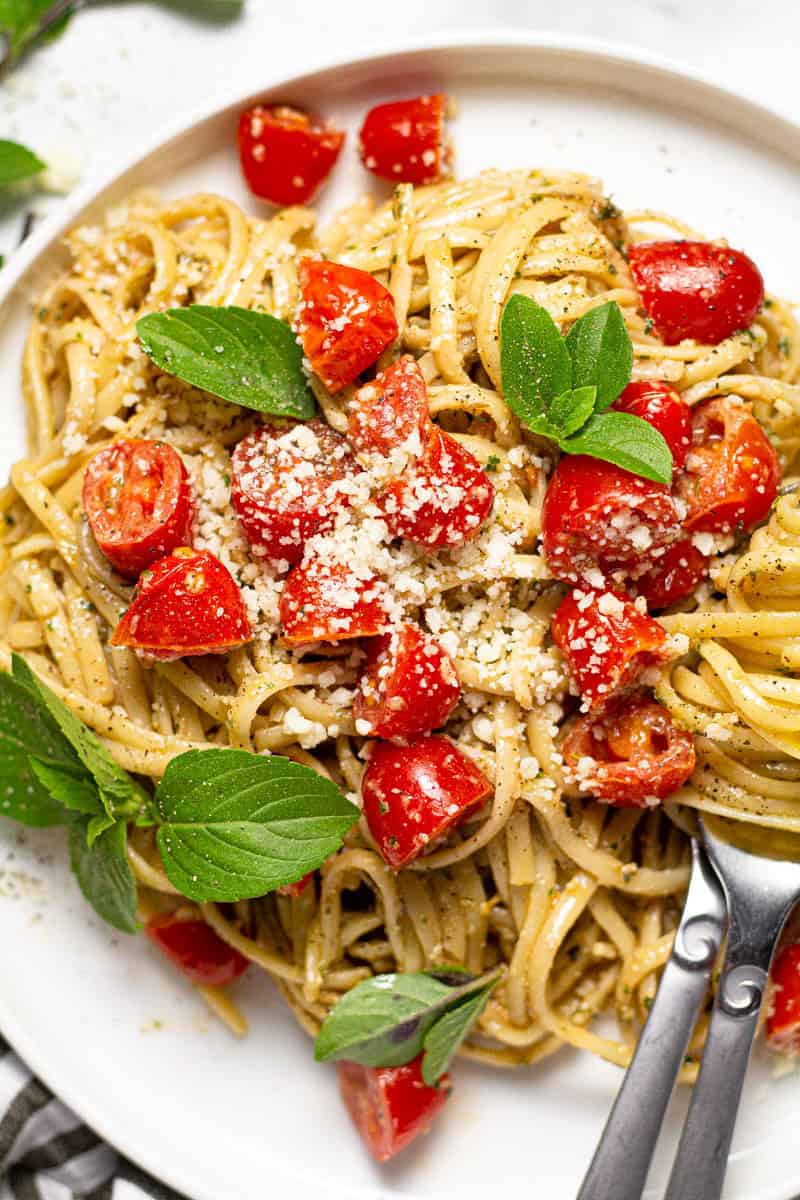 White plate with creamy pesto pasta with tomatoes 