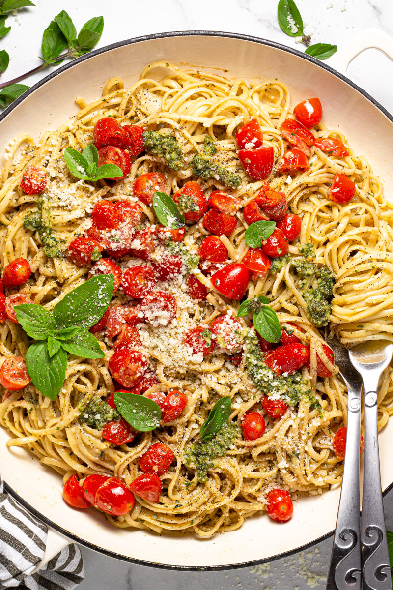 Large white pan filled with linguine tossed in a creamy pesto sauce with tomatoes