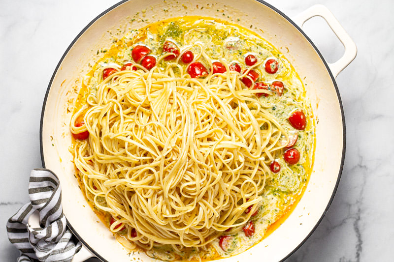 Large white pan with cooked linguine on top of creamy pesto sauce