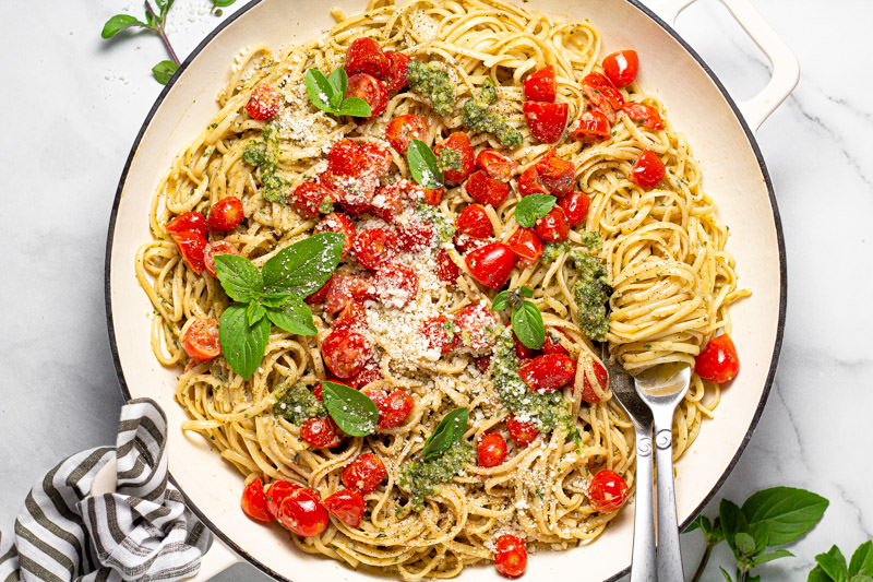 Large white pan filled with linguine tossed in a creamy pesto sauce with tomatoes