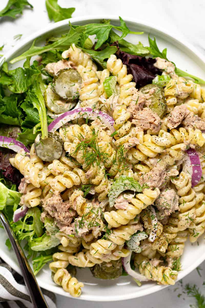 White plate filled with homemade tuna pasta salad garnished with fresh dill 