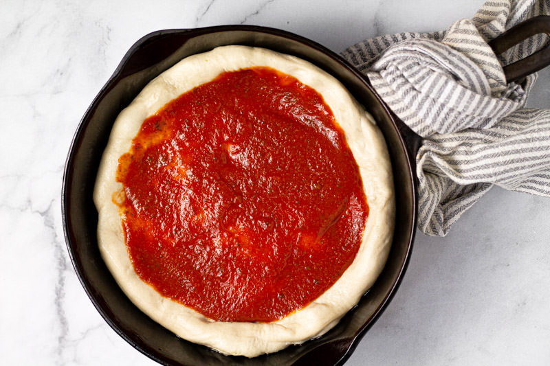 Pizza dough with pizza sauce in a cast iron skillet