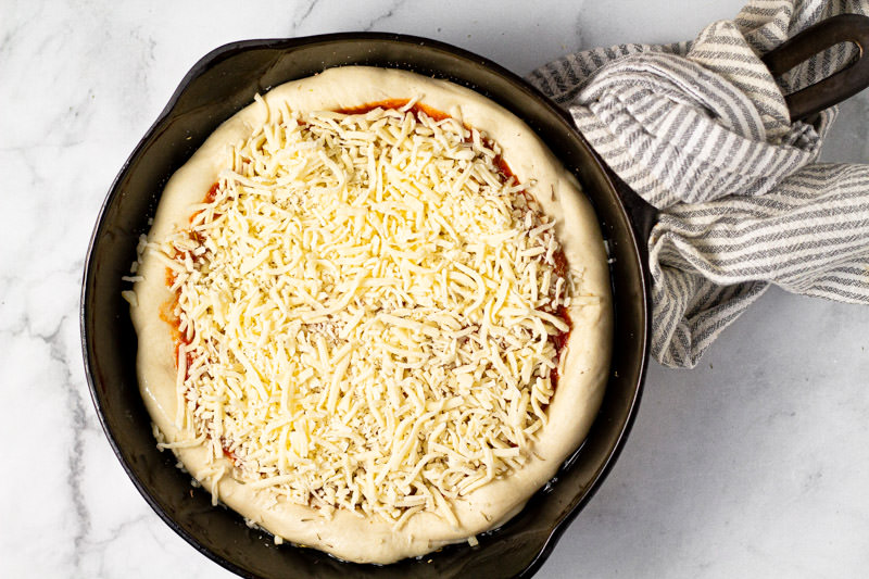 Cast iron skillet with an unbaked deep dish cheese pizza in it 
