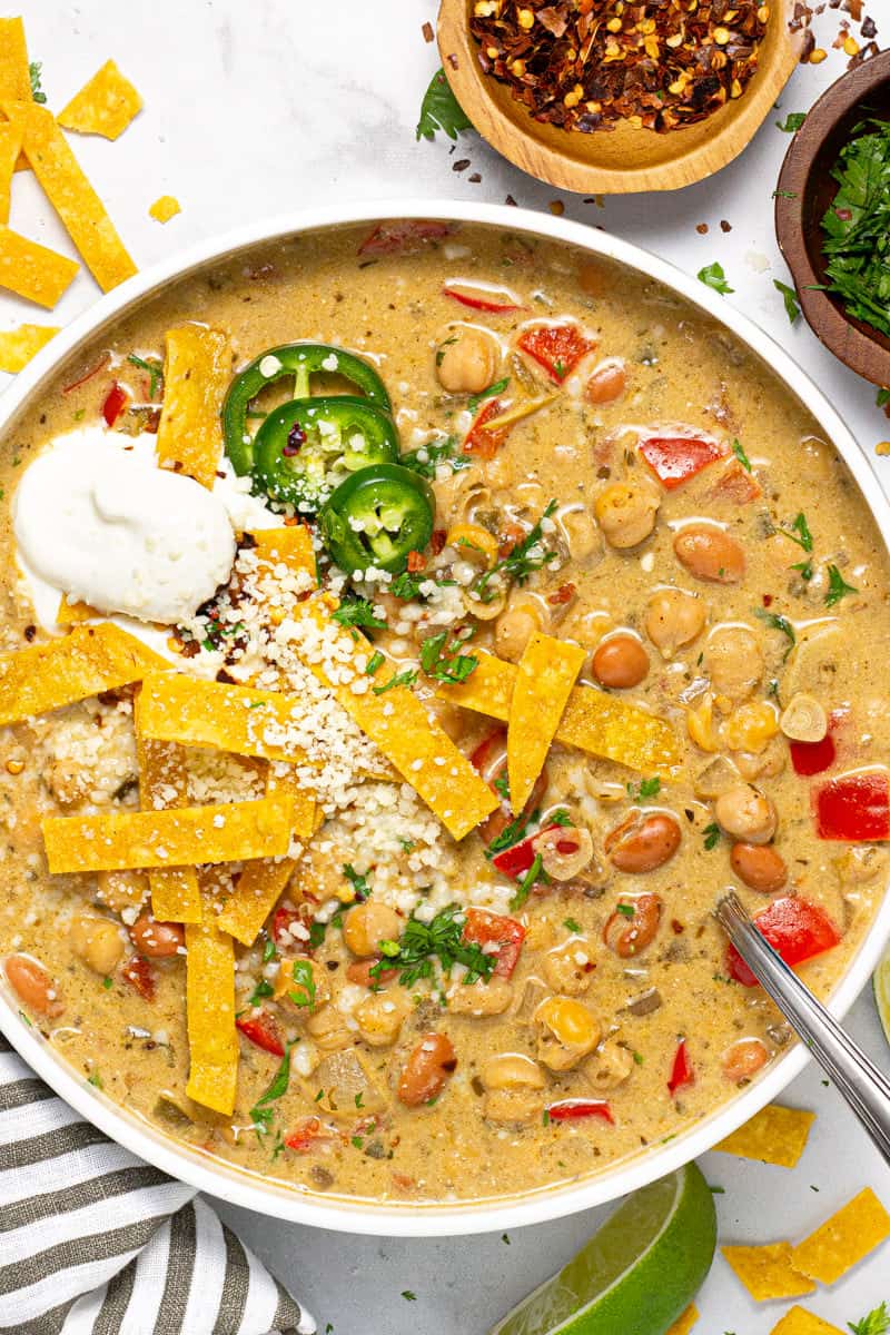 Over head shot of a white bowl of chickpea chili garnished tortilla strips and cotija cheese