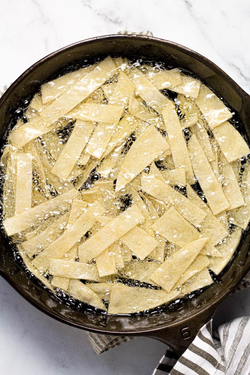 Cast iron pan with tortilla strips frying in oil
