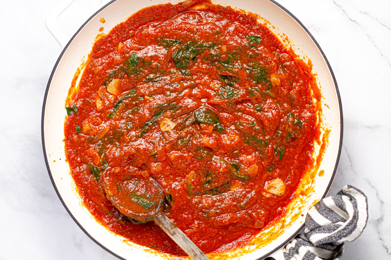 Large white pan with spaghetti sauce and wilted spinach 
