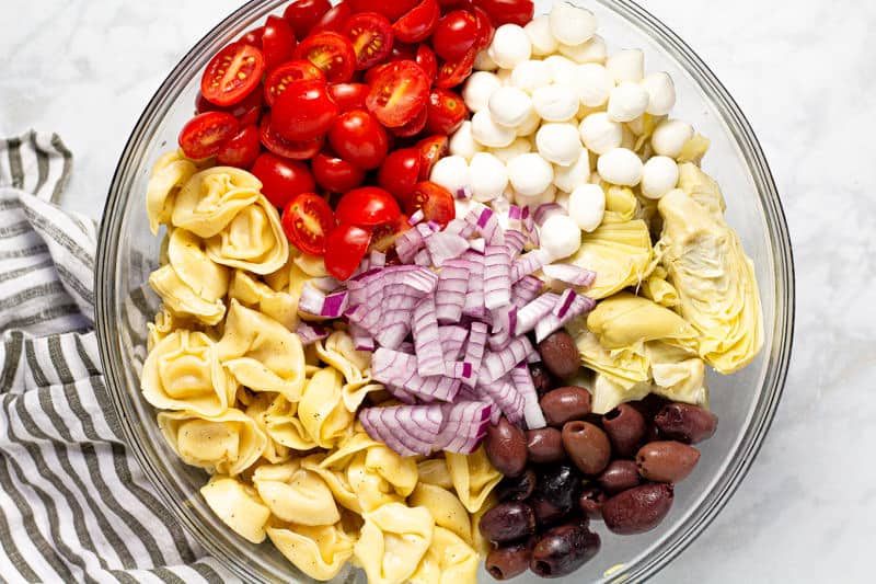Large glass bowl filled with ingredients to make basil pesto pasta salad