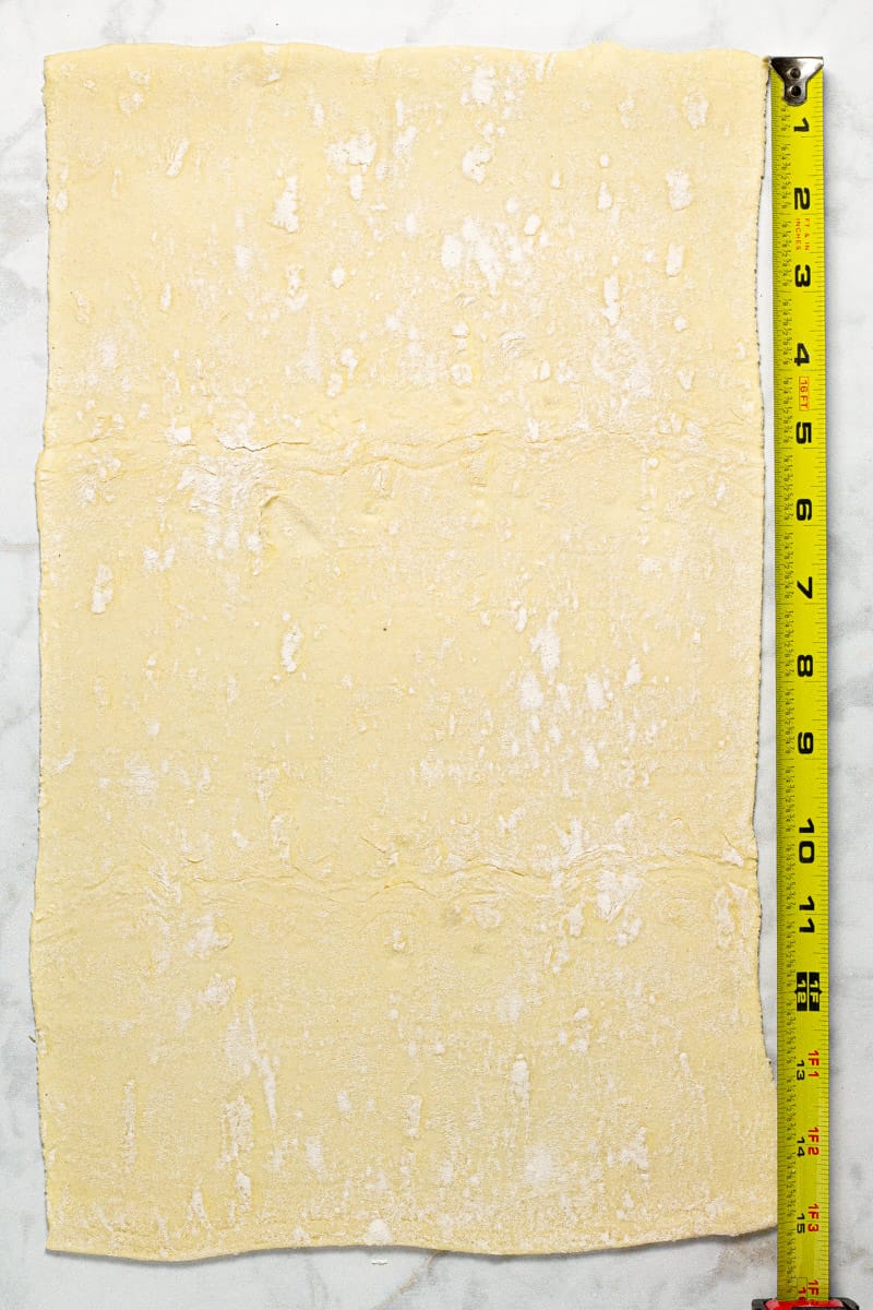 Gray marble counter top with rolled out puff pastry and a tape measure pulled out next to it
