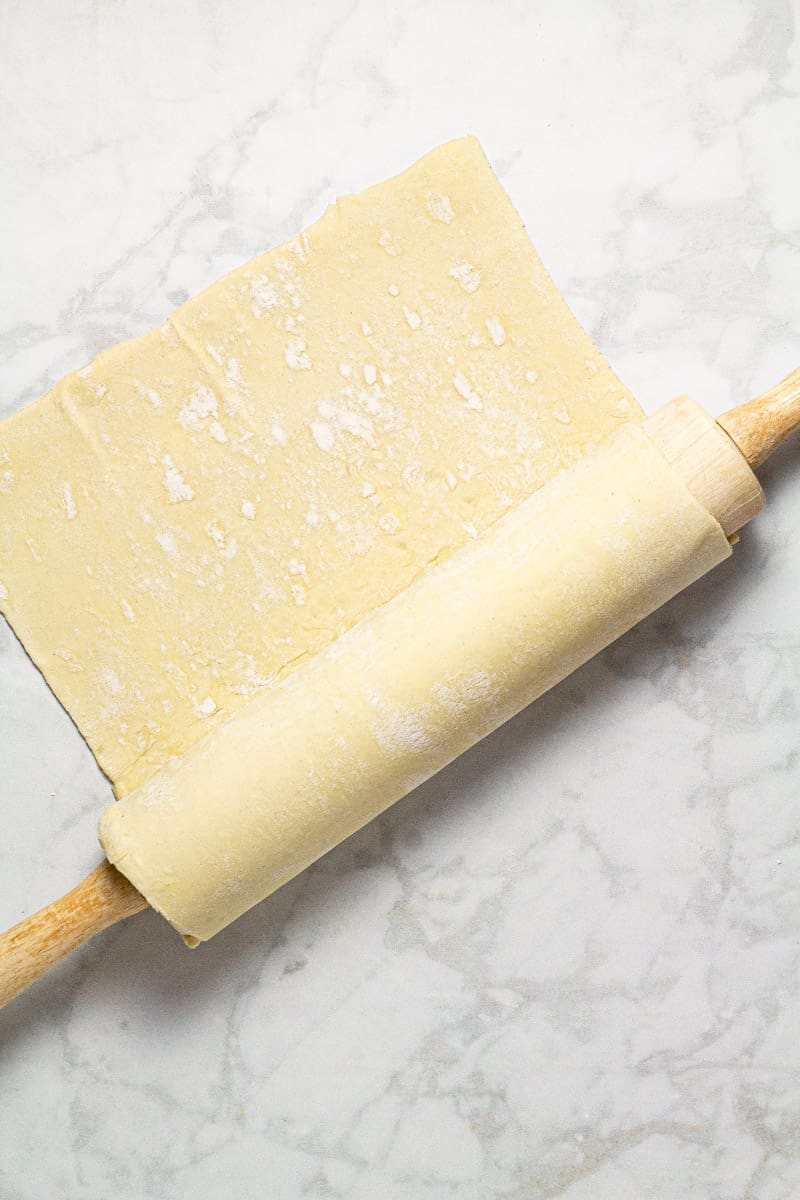 Gray marble counter top with puff pastry dough wrapped around a wooden rolling pin