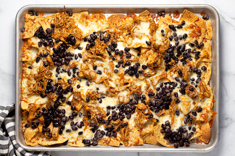 Baking sheet pan with freshly baked shredded chicken and black bean nachos