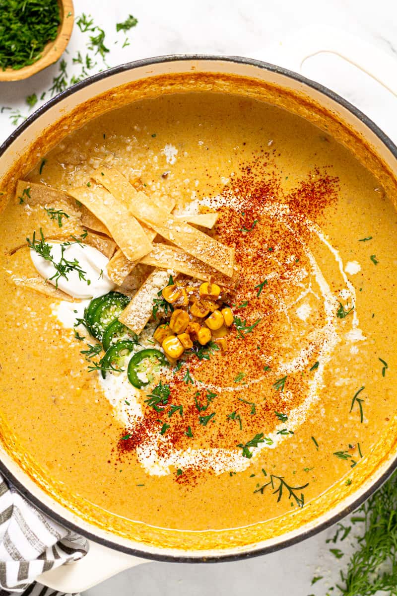 Large white pot of creamy corn soup garnished with tortilla strips
