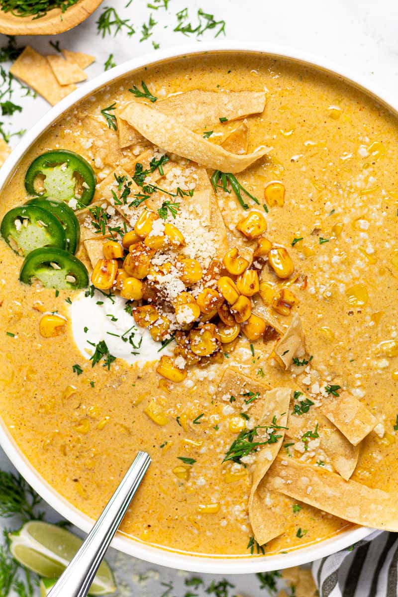 Large white bowl of creamy corn soup garnished with tortilla strips