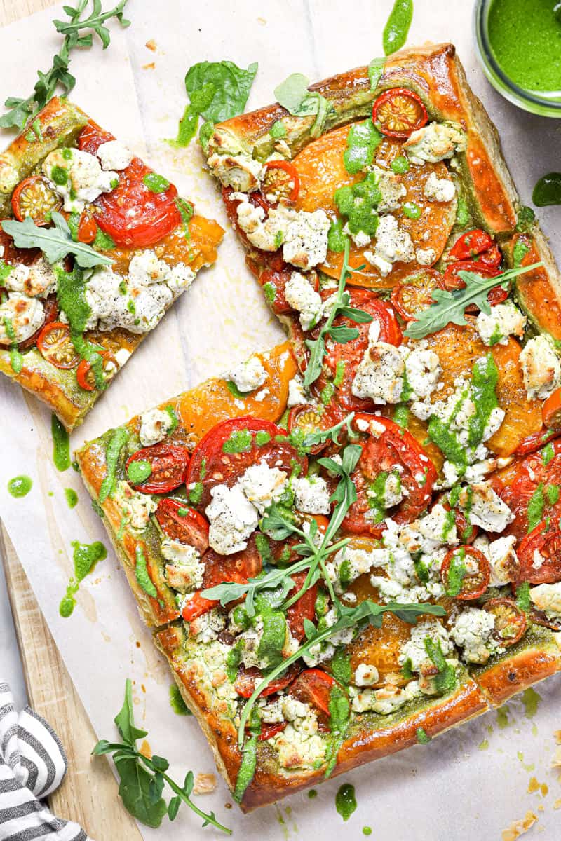 Overhead shot of a tomato puff pastry tart drizzled with homemade pesto