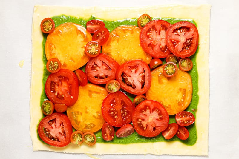 Sheet of puff pastry topped with pesto and sliced tomatoes