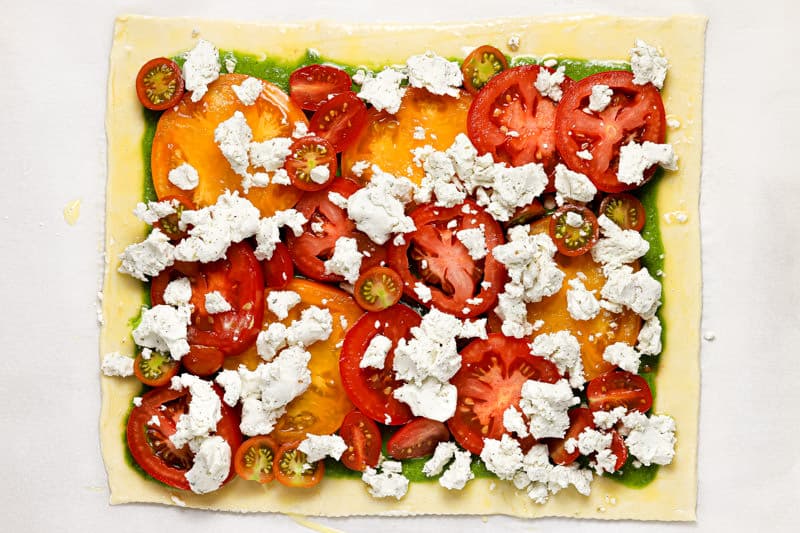 Unbaked puff pastry tomato and goat cheese tart on a baking sheet