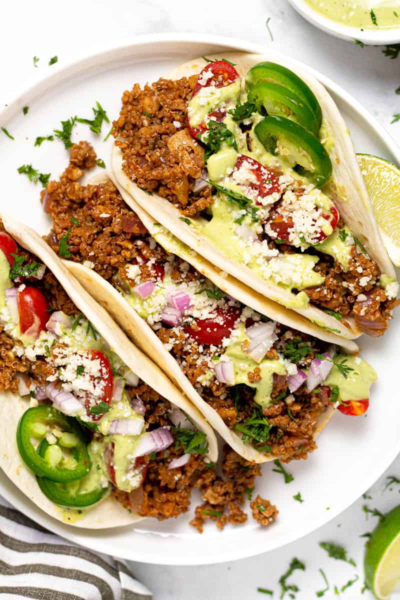 White plate with vegan tacos garnished with avocado sauce and fresh cilantro 