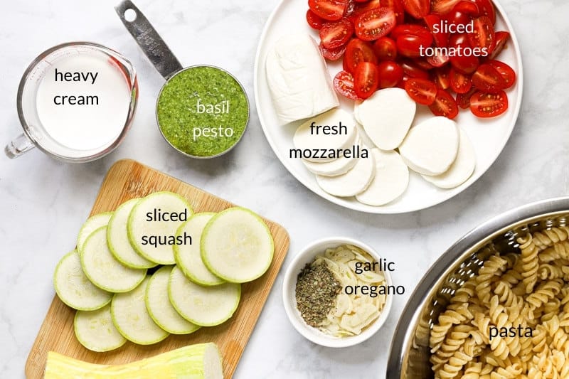 White marble counter top with ingredients to make pesto tomato pasta bake