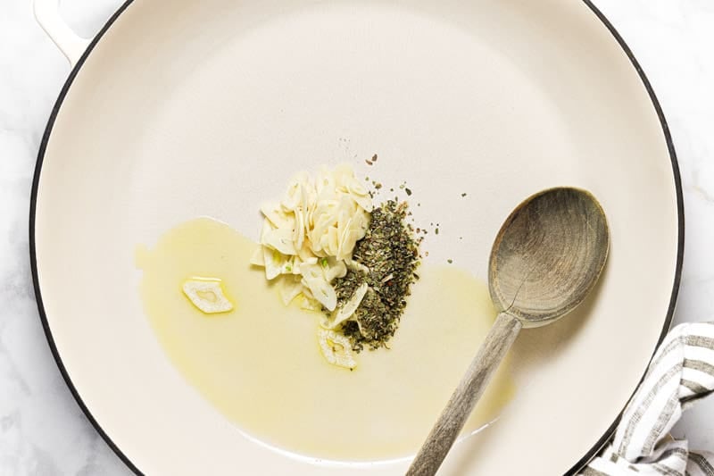 Large white pan with olive oil sliced garlic and dried oregano