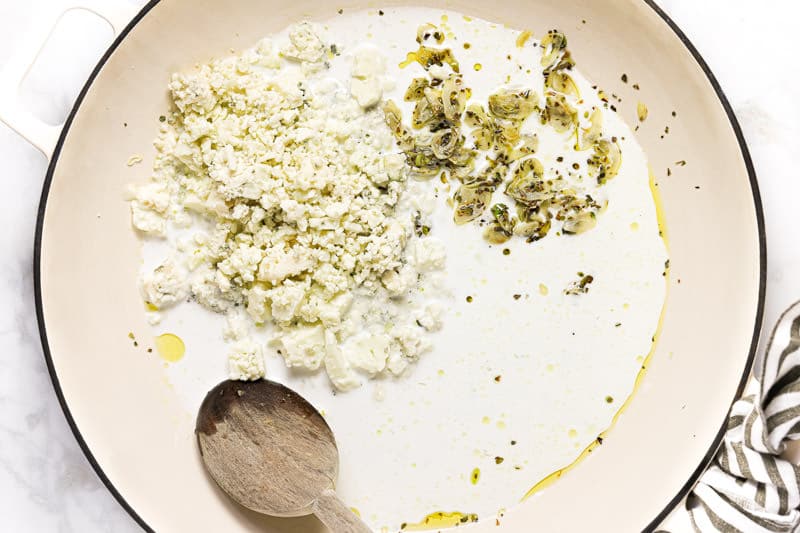 Large white pan with heavy creamy sauteed garlic and crumbled blue cheese in it