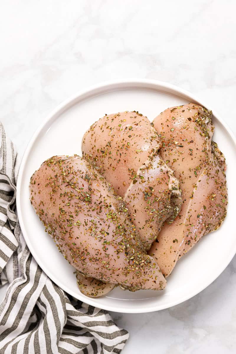 Large white plate with raw chicken breast seasoned with dried spices