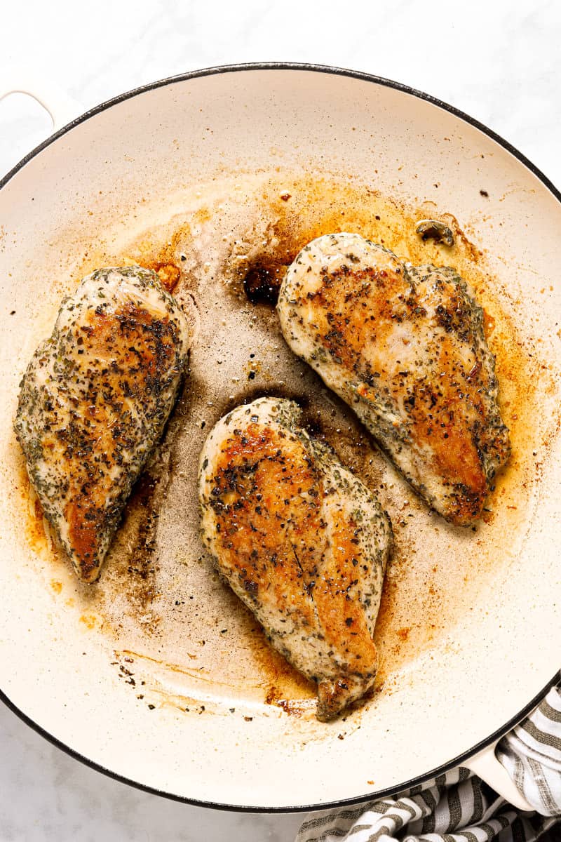 Large white pan with sauteed chicken breast in it