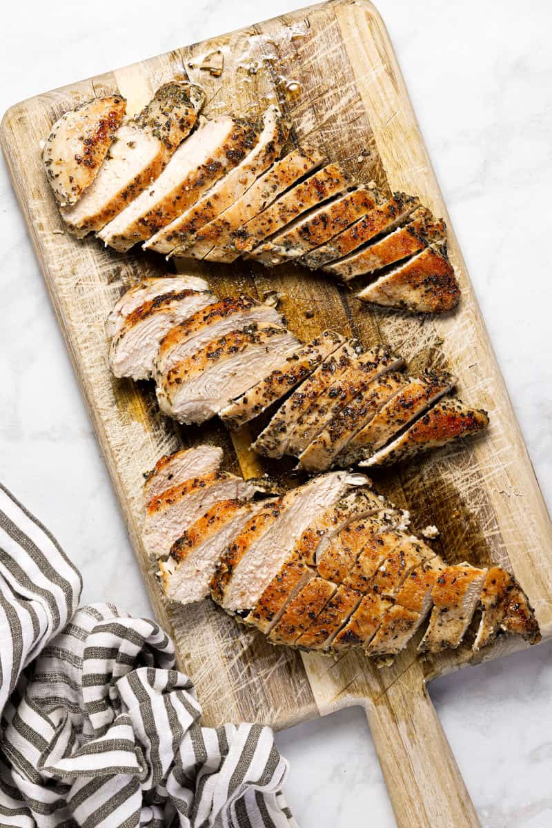 Wooden cutting board with sliced sauteed chicken on it