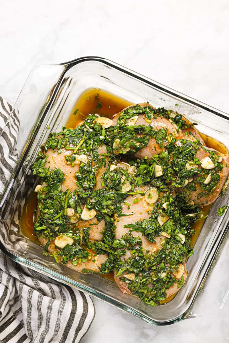 Square glass baking dish with raw chicken breast marinating in cilantro lime marinade