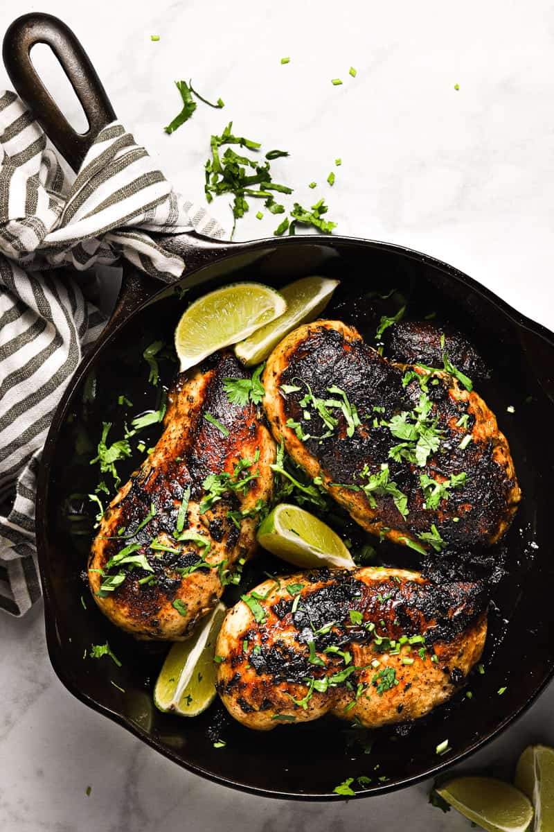 Overhead shot of a cast iron pan with golden brown sauteed cilantro lime chicken garnished with lime wedges