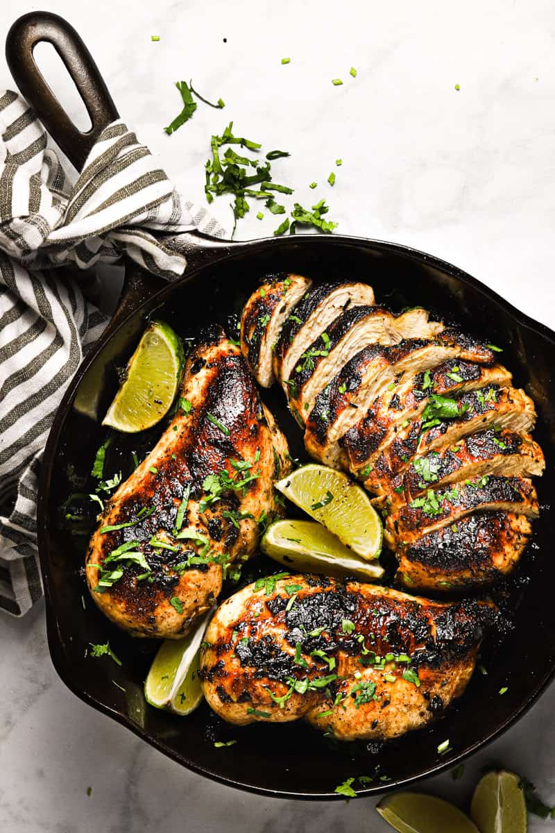 Overhead shot of a cast iron pan with golden brown sauteed cilantro lime chicken garnished with lime wedges