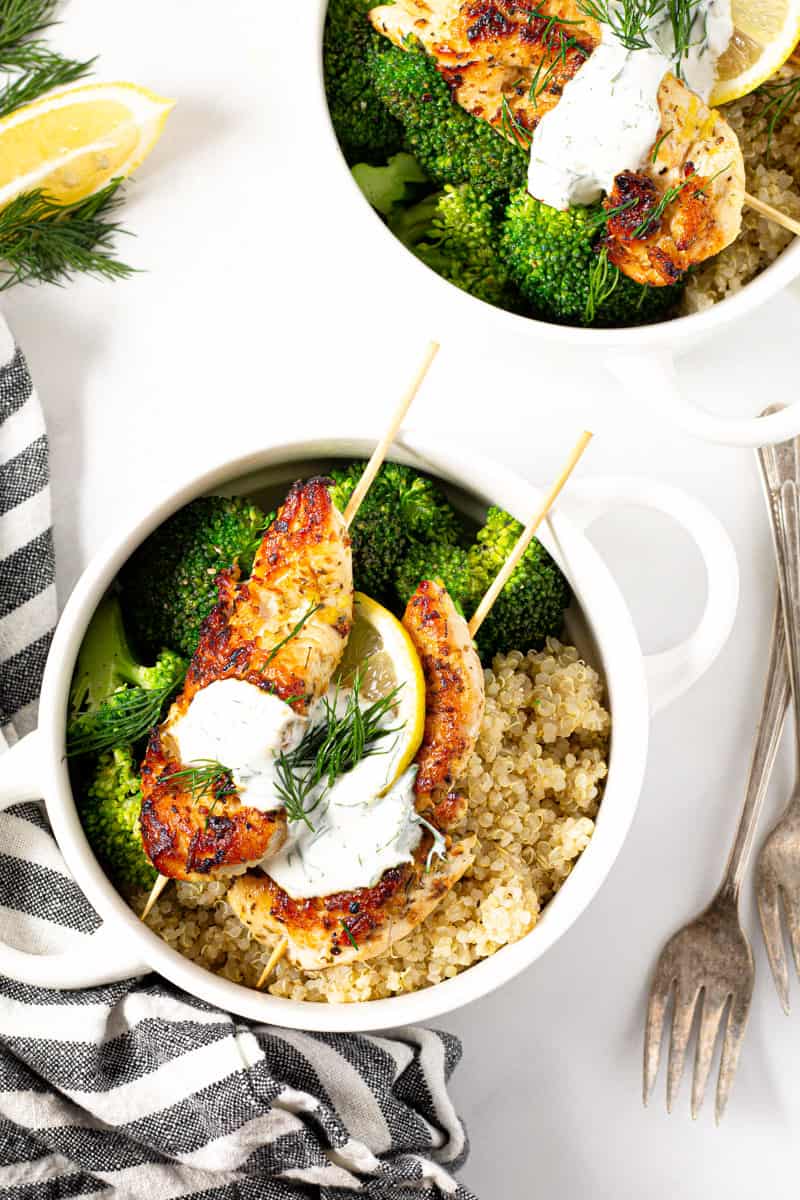 Two white bowls filled with Greek chicken kebabs quinoa and broccoli
