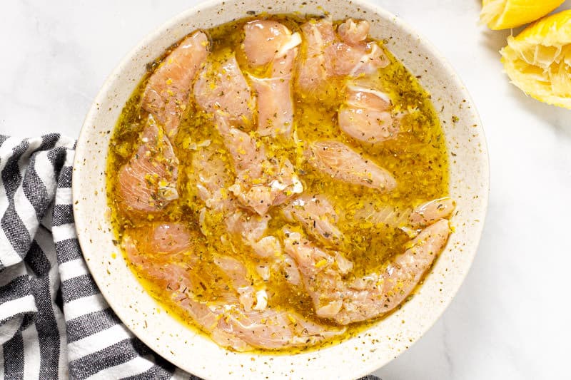 Raw chicken tenders marinating in a bowl 