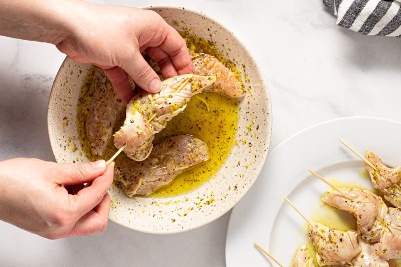 Two hands threading chicken onto a wooden skewer