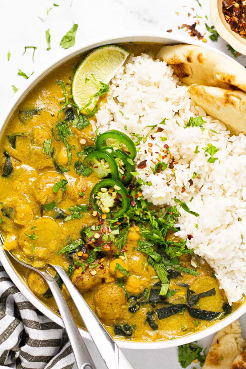 Large white bowl filled with rice and vegan curry garnished with fresh chopped cilantro