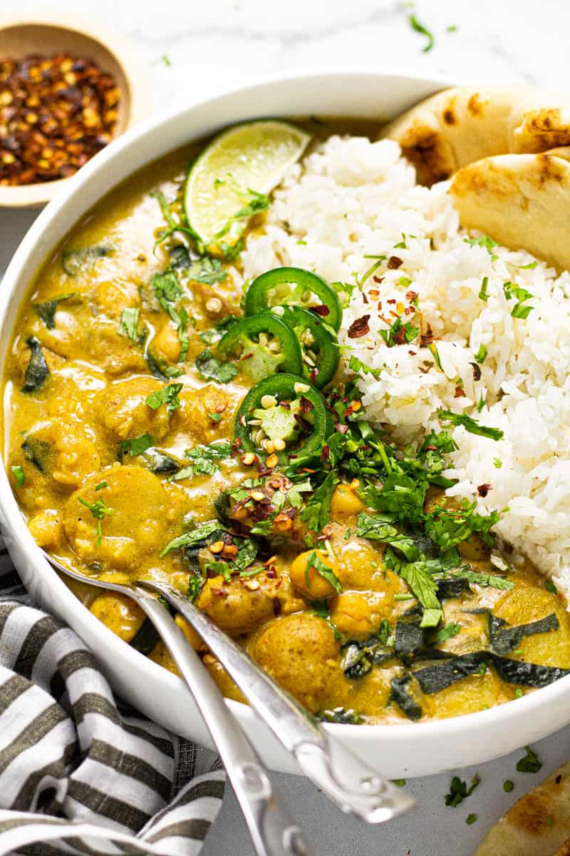 Close up shot of a large white bowl filled with rice and vegan curry garnished with fresh chopped cilantro