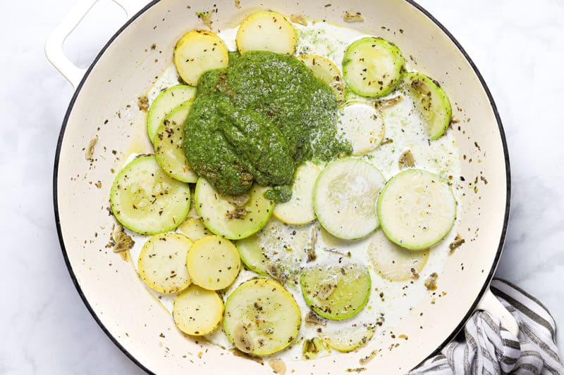 Large white pan with sliced squash pesto and heavy cream 