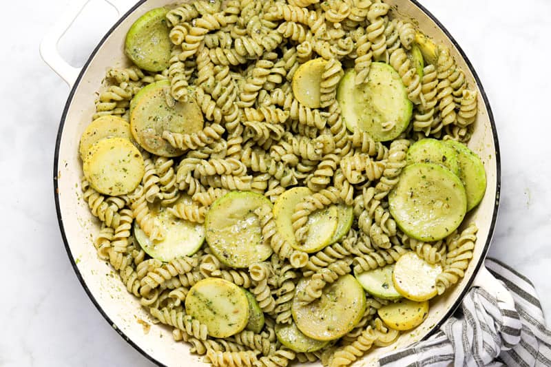 Large white pan with pesto pasta and sliced squash 