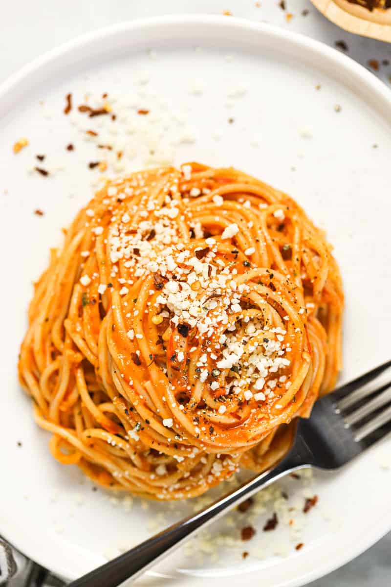 White plate with twirled spaghetti tossed in tomato sauce