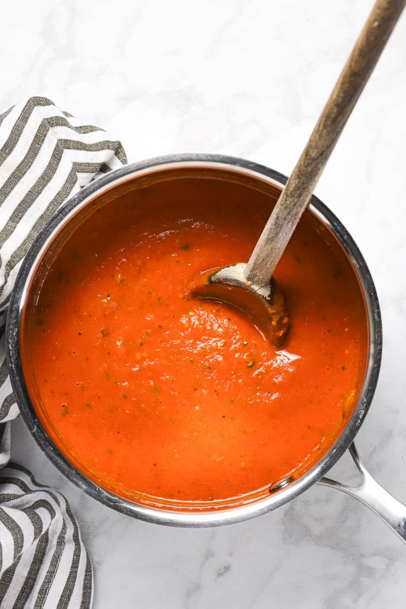 Small silver pot with creamy tomato sauce and a wooden spoon