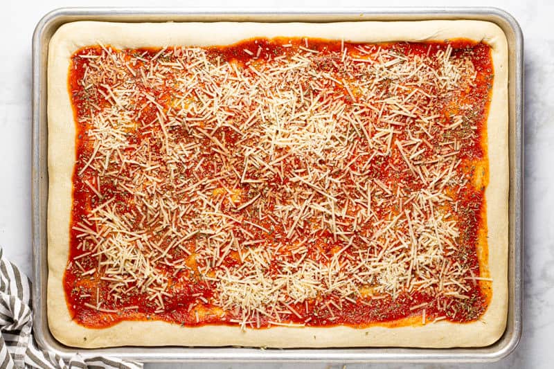 Pizza dough topped with sauce and cheese on a baking sheet