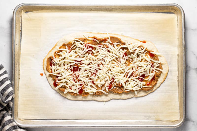 Flatbread crust on a baking sheet topped with refried beans and cheese