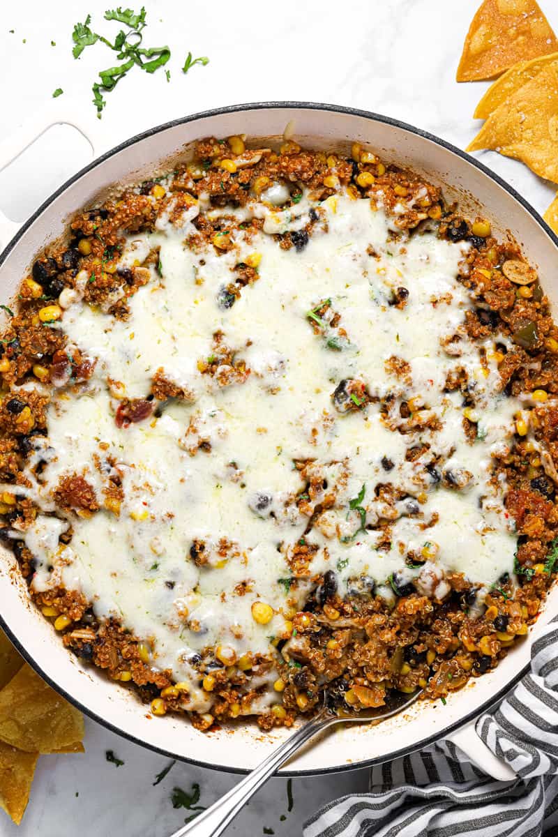 Mexican quinoa in a large white pan with melted pepper jack cheese on top