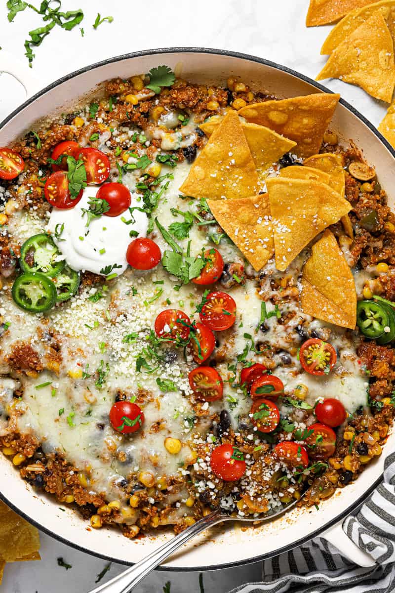 Large white pan filled with Mexican quinoa garnished with sour cream tomatoes and chips
