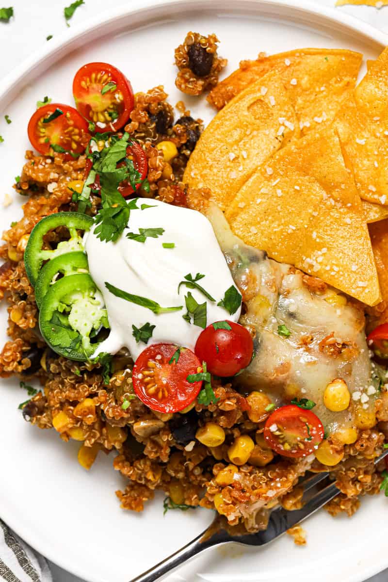 White plate with a scoop of Mexican quinoa garnished with sour cream tomatoes and chips