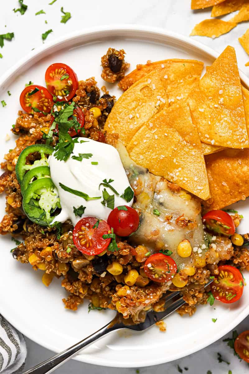 White plate with a scoop of Mexican quinoa garnished with sour cream tomatoes and chips