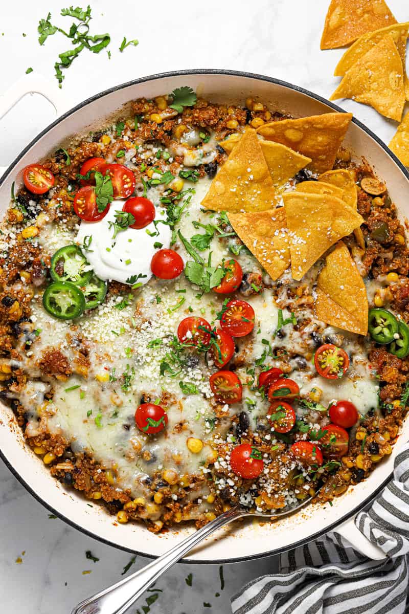 Large white pan filled with Mexican quinoa garnished with sour cream tomatoes and chips