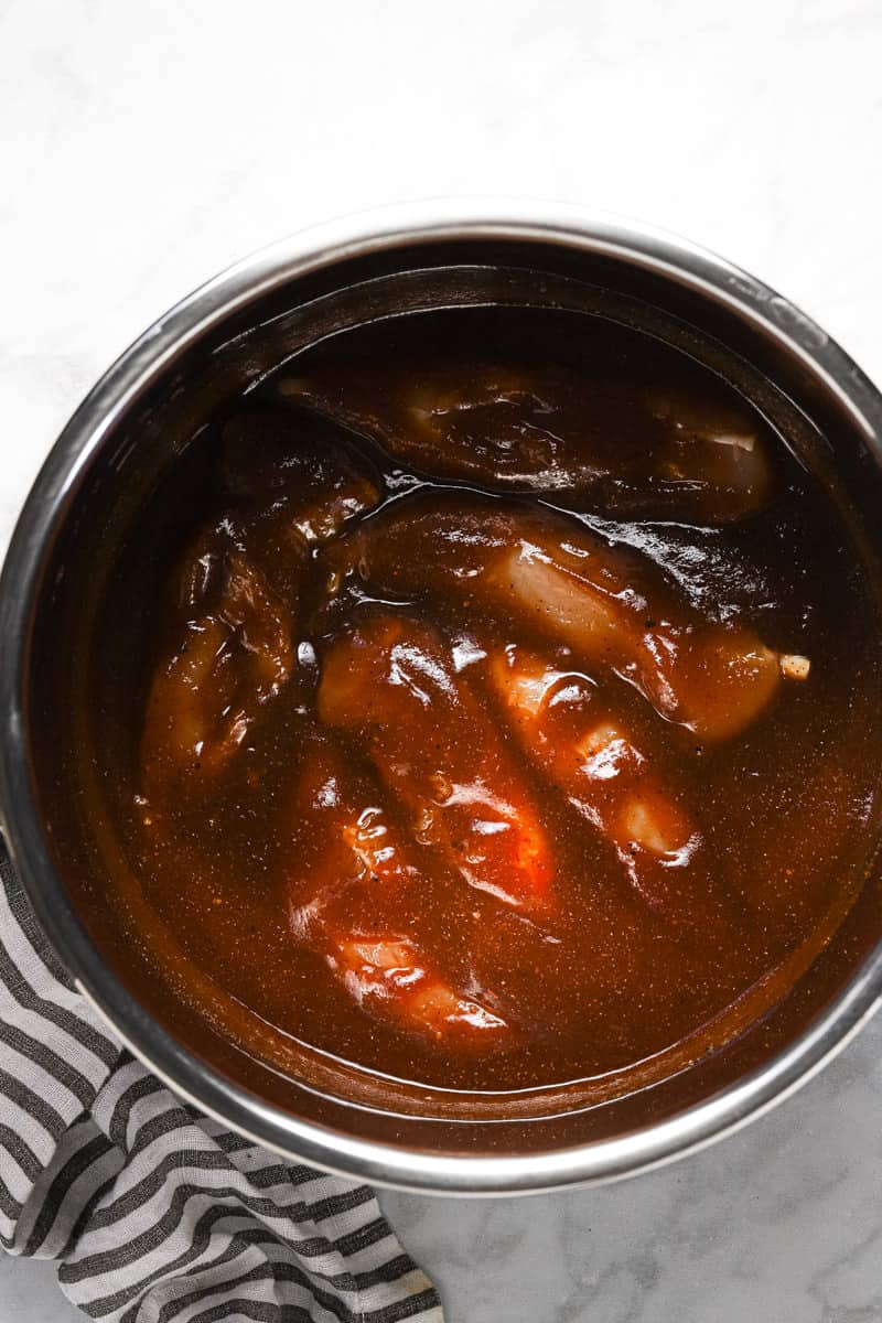 Instant pot insert with raw chicken breast and BBQ sauce in it